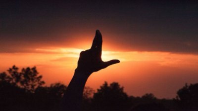 A hand held up to the sunset in the "L" for GVSU Lakers gesture.